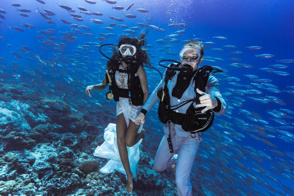 A couple scuba diving underwater, surrounded by schools of fish and colorful coral, showcasing the vibrant marine life of Seychelles.